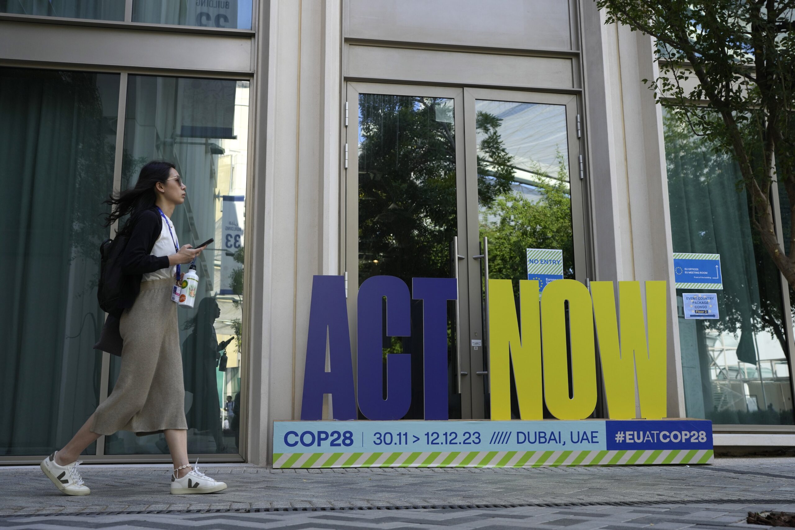 A woman walks near a sign that reads "act now" at the COP28 U.N. Climate Summit, Sunday, Dec. 10, 2023, in Dubai, United Arab Emirates. (AP Photo/Rafiq Maqbool)