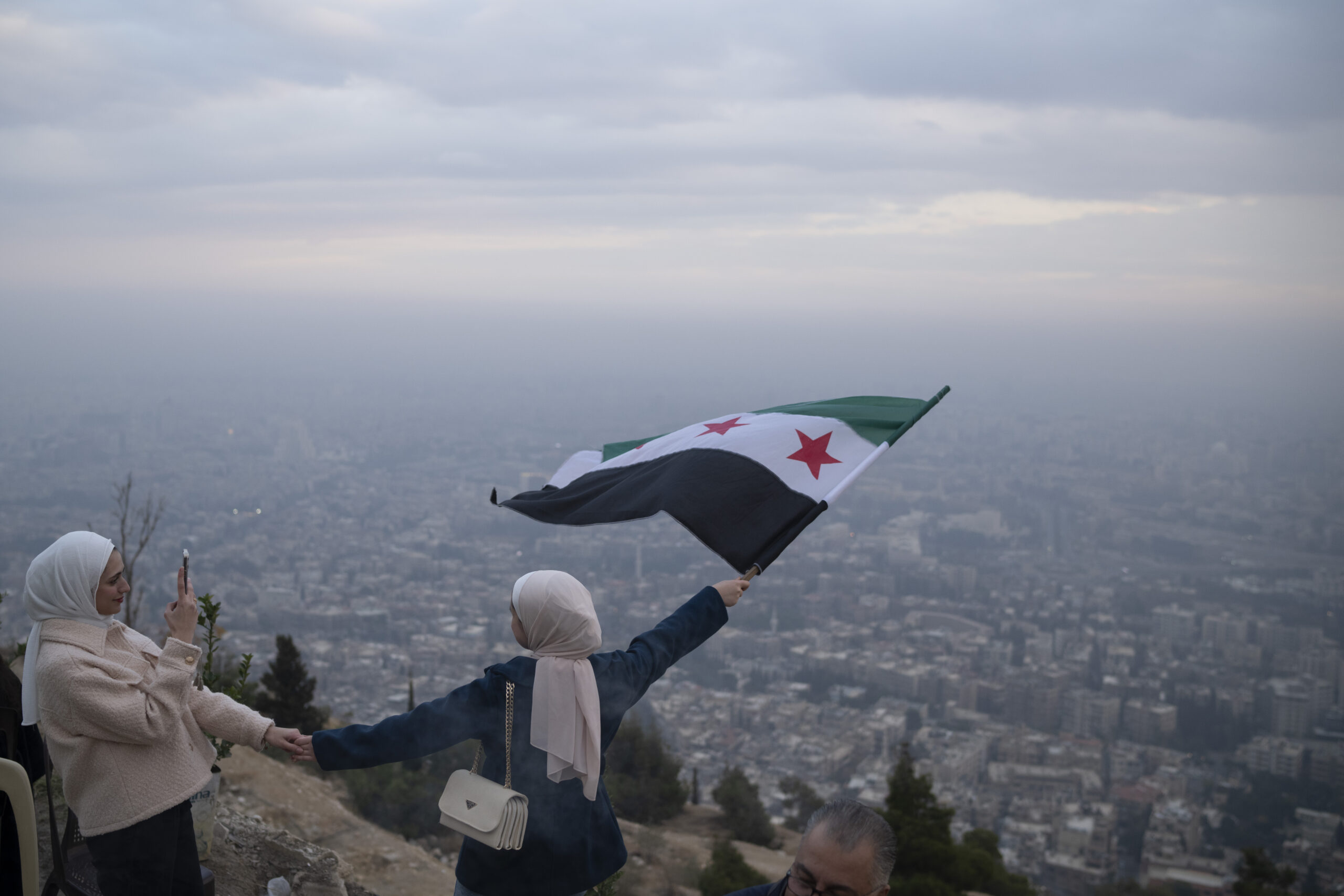 A young woman poses for a photo waving a Syrian "revolutionary" flag at a lookout area on Mount Qasioun in Damascus, Syria, December 21. (AP Photo/Leo Correa)