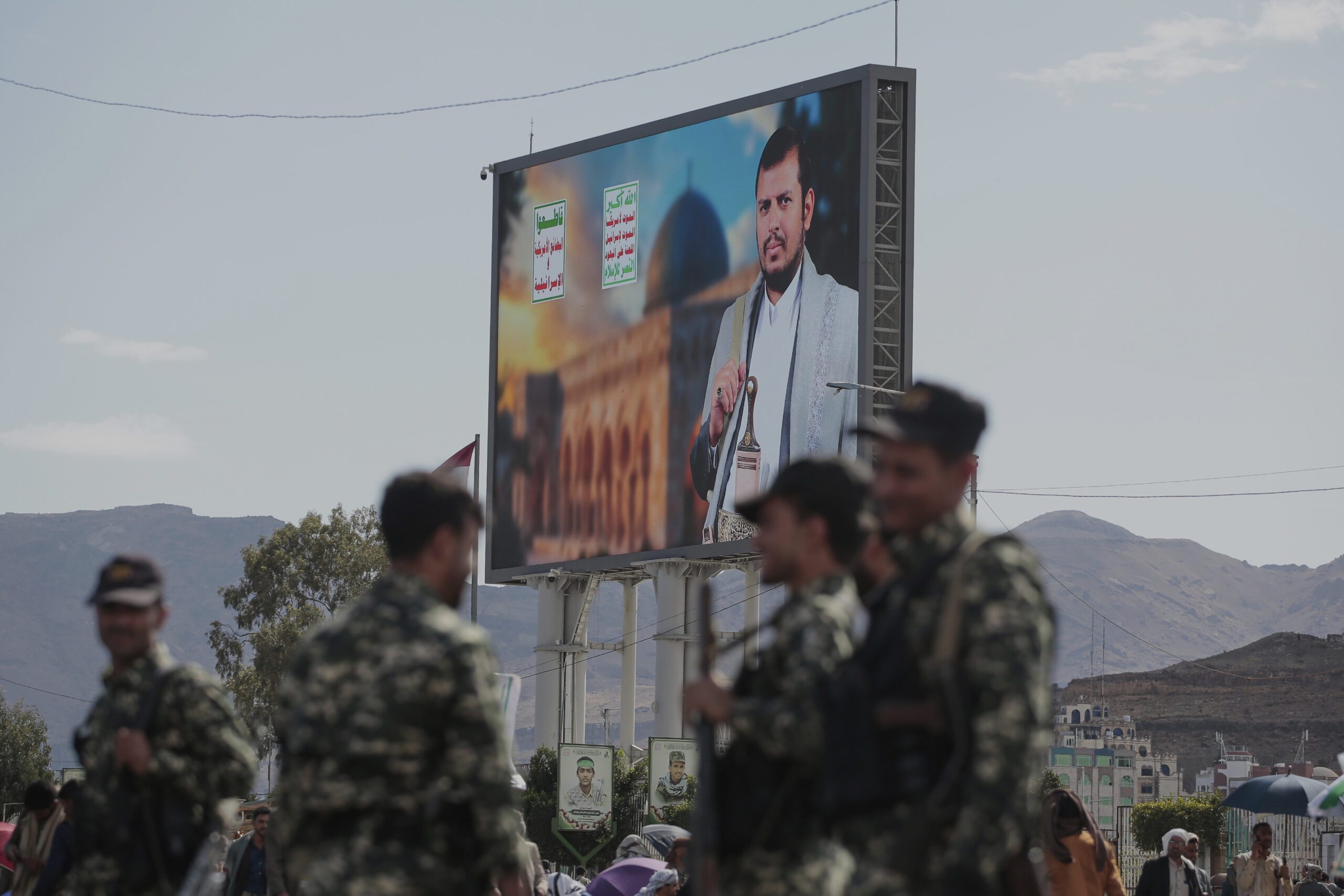 Houthi security officers stand next to a street billboard displaying a picture of Abdul Malik al-Houthi, the leader of the Houthi movement, in Sanaa, Yemen, March 17. (AP Photo/Osamah Abdulrahman)