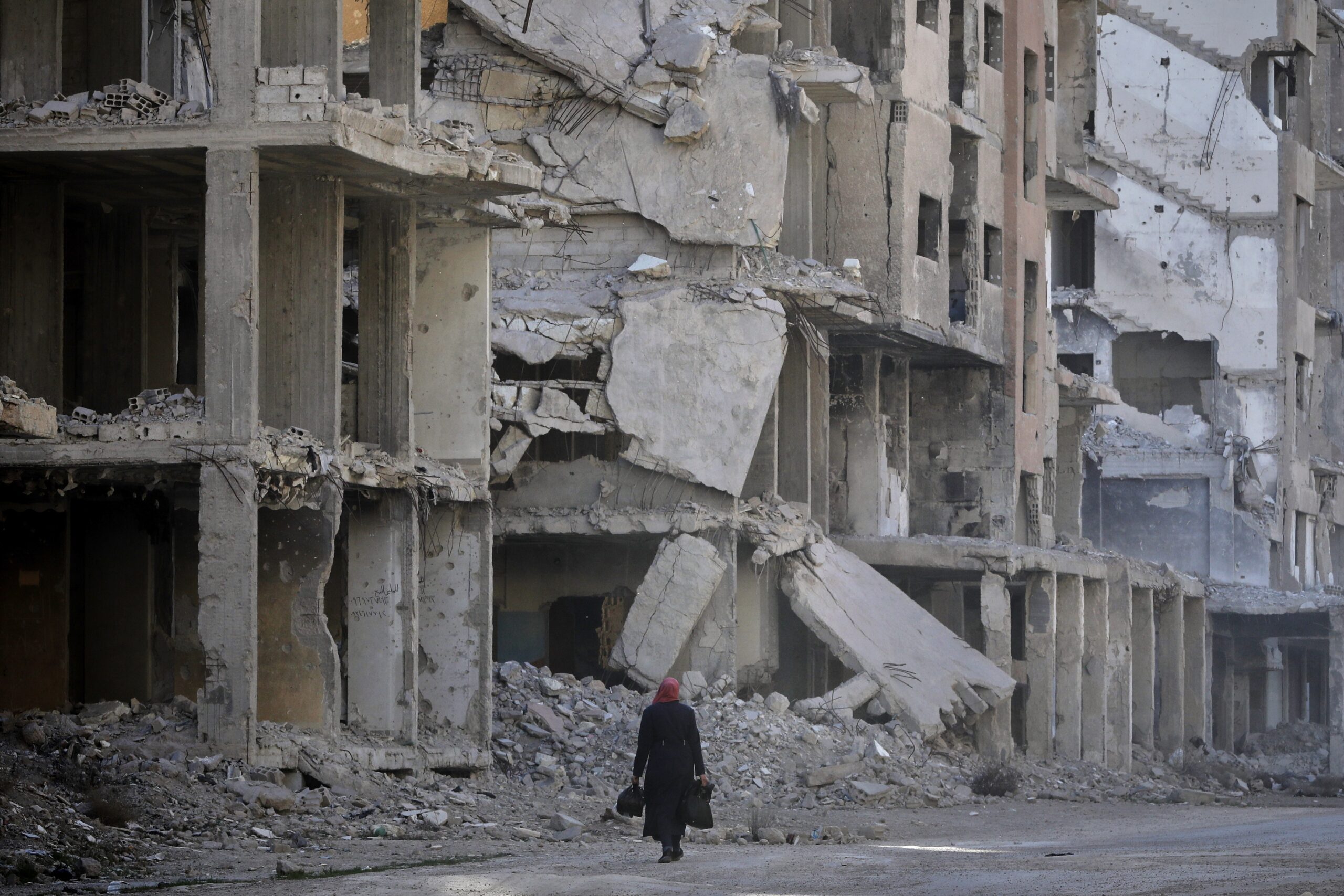 A woman walks past damaged apartment buildings in Daraya, Syria, March 12. (AP Photo/Omar Sanadiki)